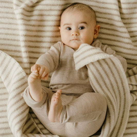 Baby in a beige outfit lying on a striped blanket