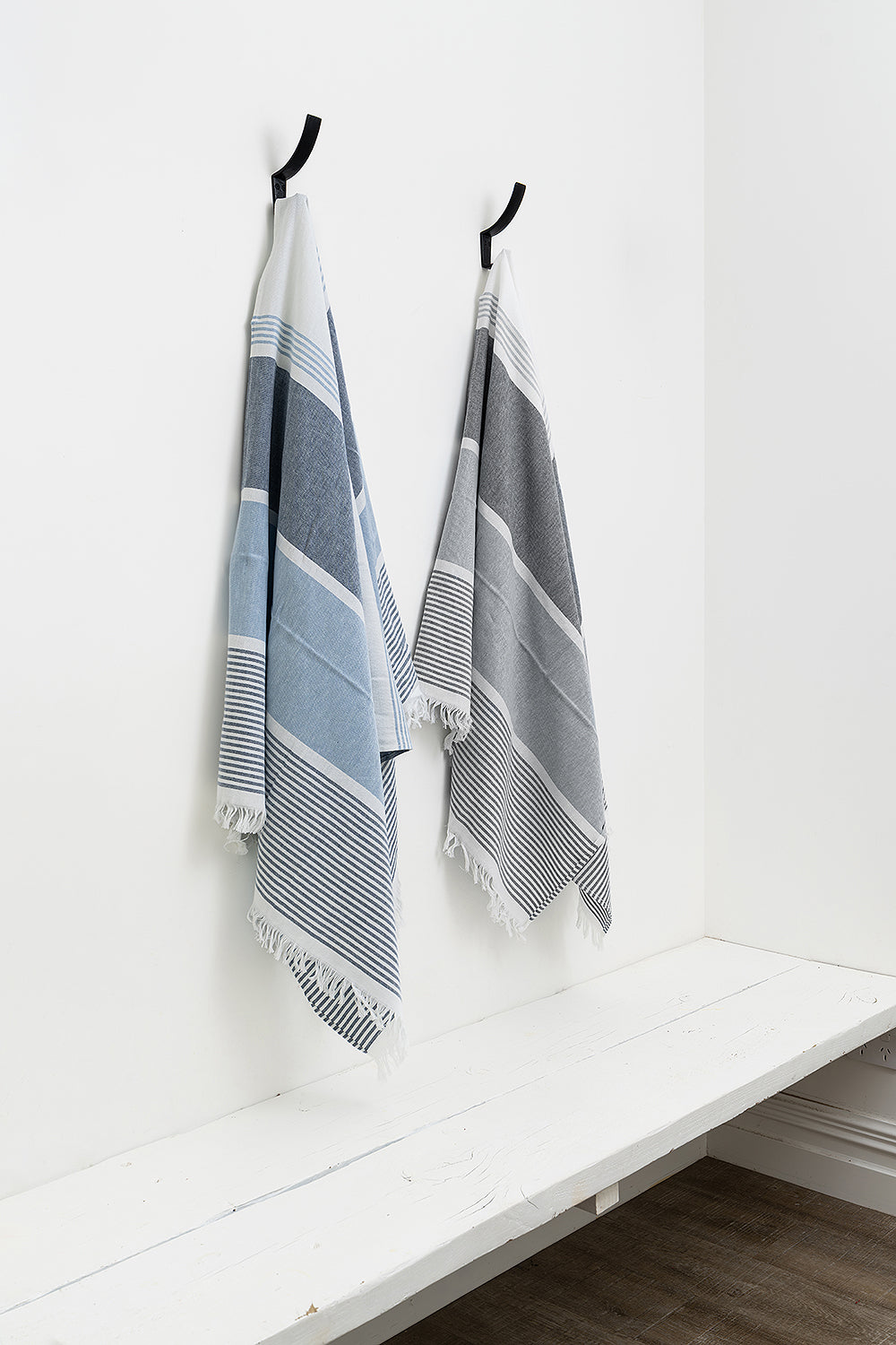 Two striped towels hanging on hooks against a white wall.