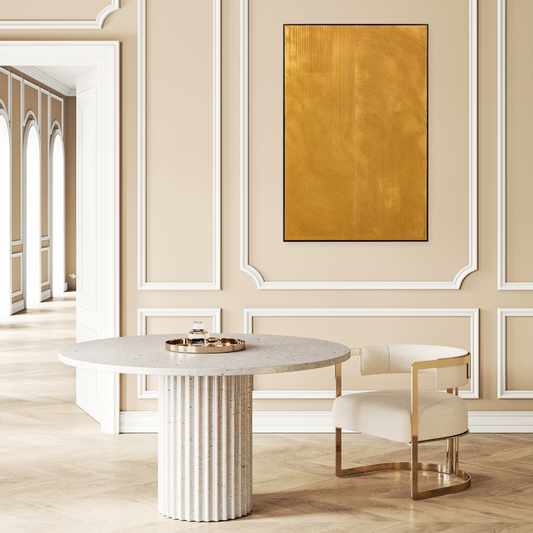 gold textured oil painting on a beige wall with panelling. Infront is a white marble round table and a gold and white fabric mid century style chair, both sitting on a pale wooden parquet floor