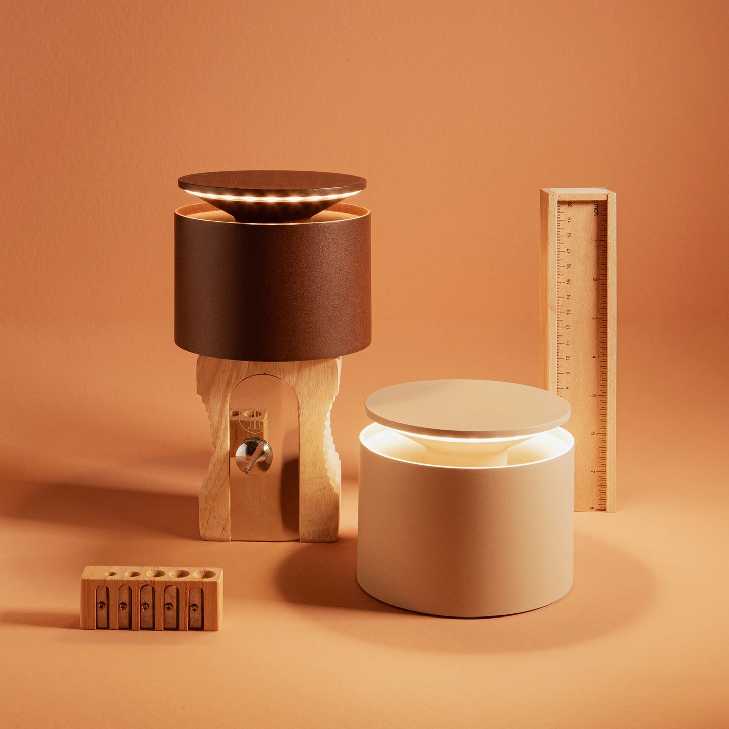 Two cylindrical lamps, one brown and one beige, on an orange background with wooden objects.