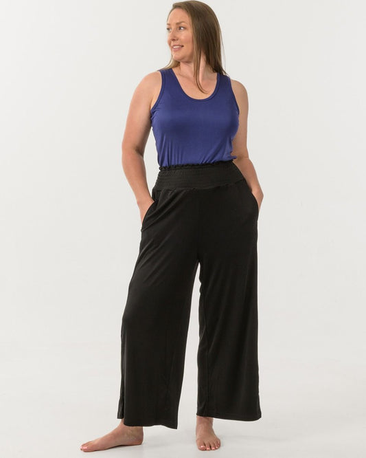 Woman wearing a blue tank top and black silk wide-leg pants on a white background