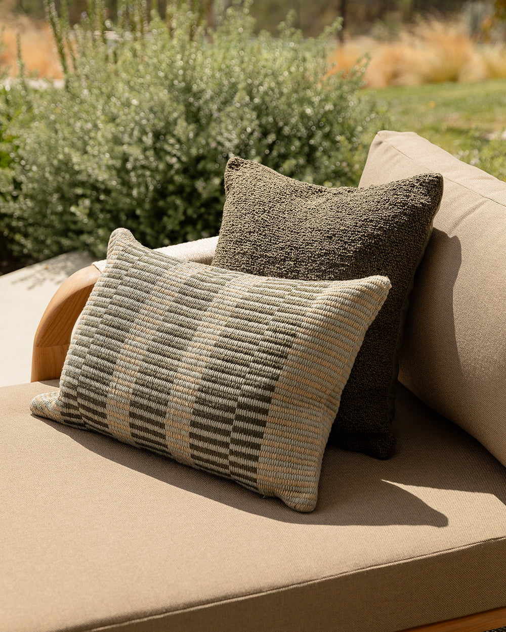Two patterned pillows on a beige outdoor sofa with a garden background