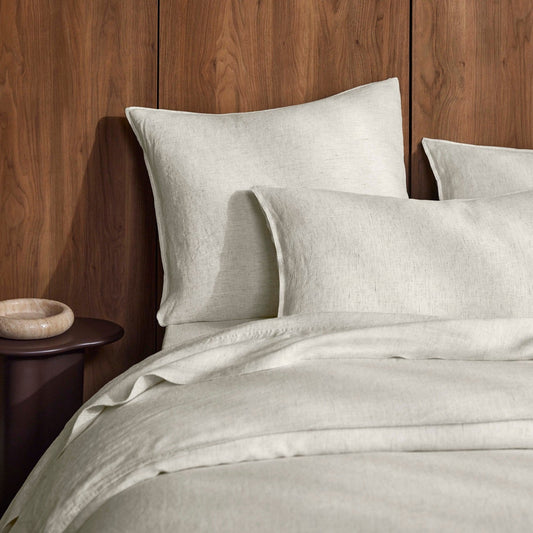 Neatly made bed with light-colored Sova bed linen against a wooden headboard.