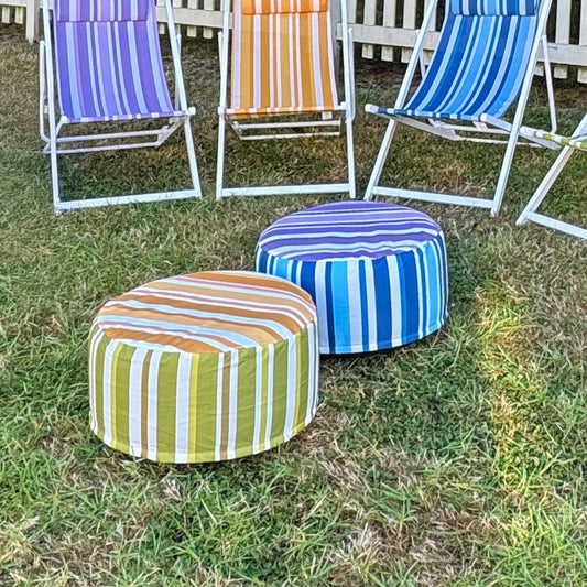 Colorful striped deck chairs and ottomans on grass with a white picket fence and tree in the background