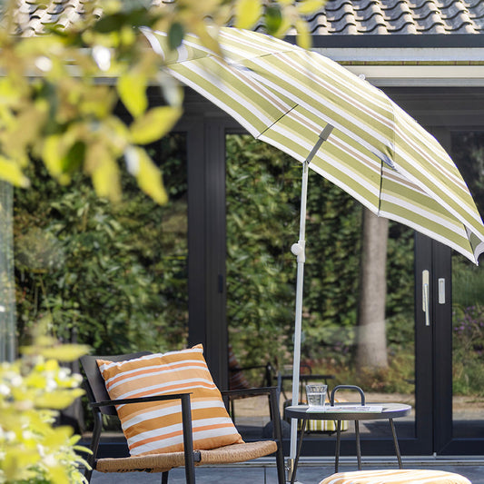Outdoor patio with striped umbrella, chair, ottoman, and table in a garden setting.