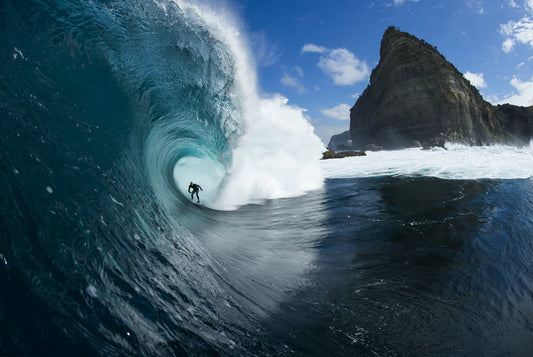 Surfer riding a large wave in the ocean with a rocky cliff in the background