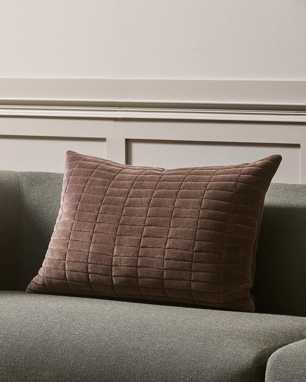 Quilted brown pillow on a gray sofa against a beige wall.