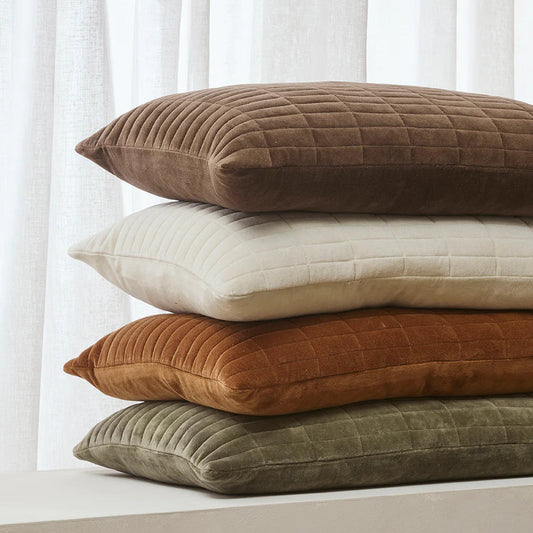 Stack of brown, beige, orange, and green textured pillows against a white curtain background.