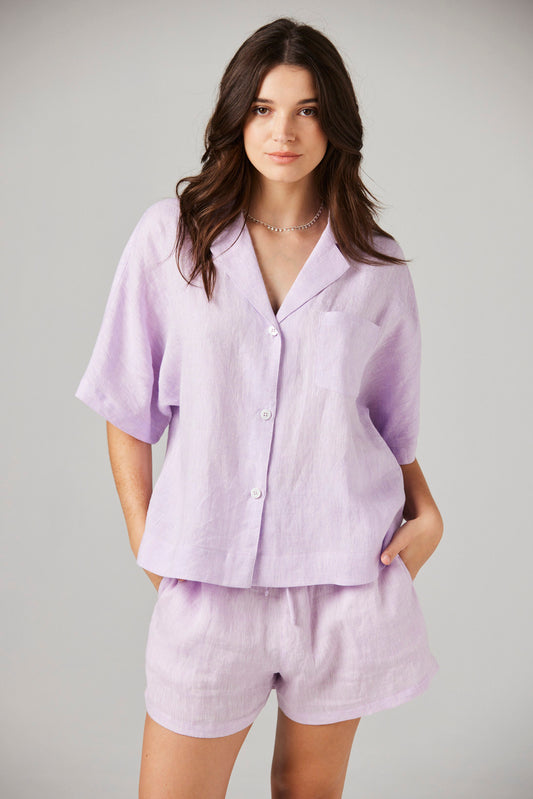 Woman wearing a llilac linen shirt and shorts set on a gray background