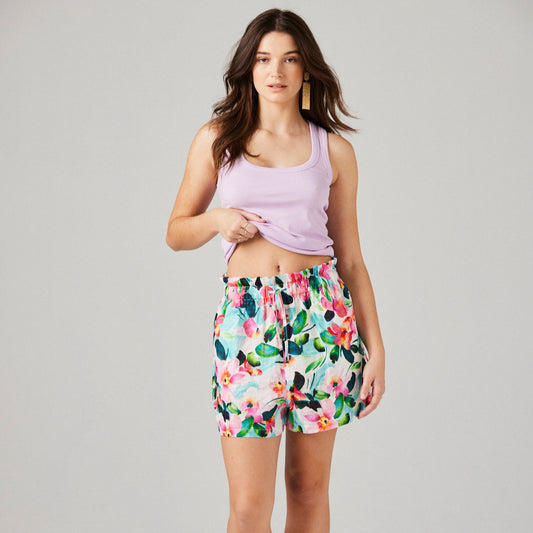 Woman wearing a light purple tank top and floral shorts on a plain background