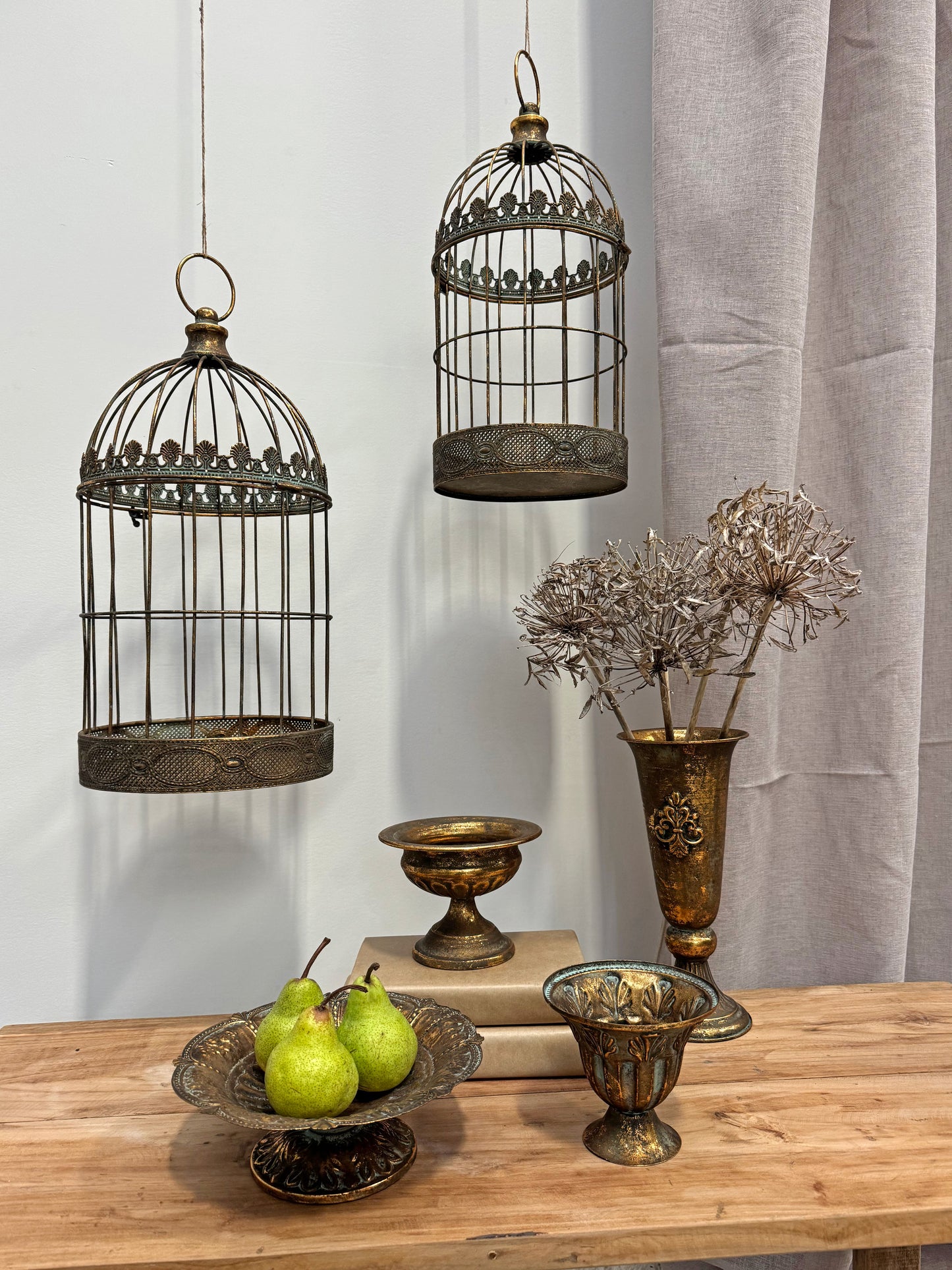 Decorative birdcages, vases, and fruit on a wooden surface with a neutral background