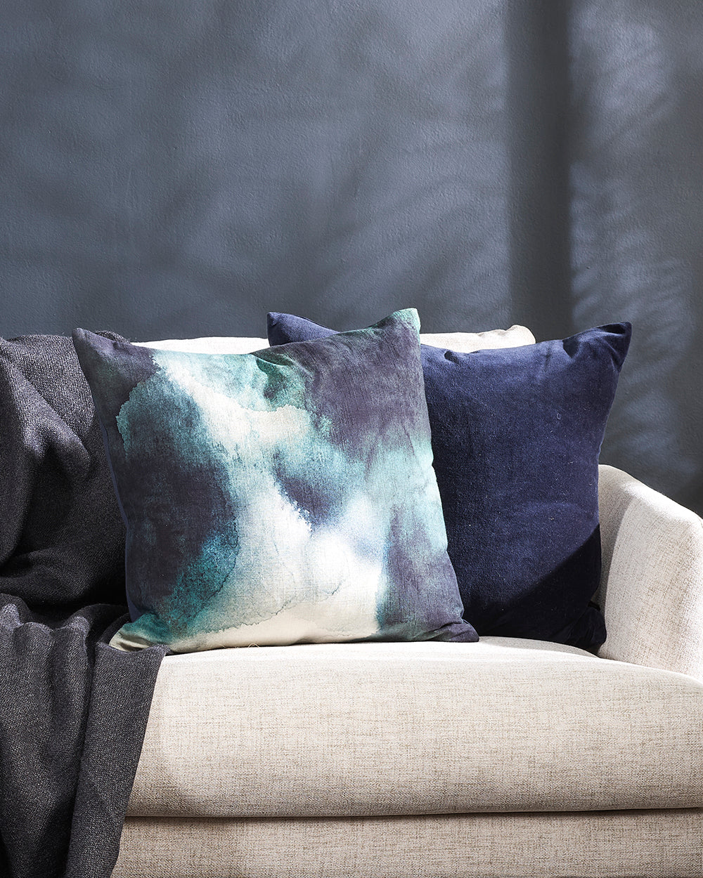 Amelia abstract blue cushion on a white sofa with a navy velvet cushion and grey throw
