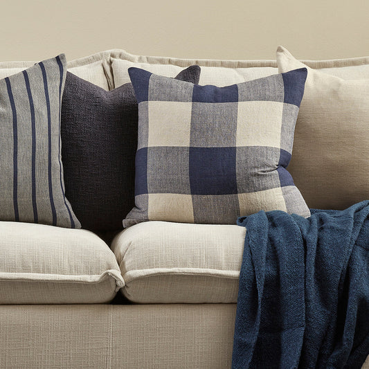 Gray sofa with decorative checked pillows and a blanket on a neutral background