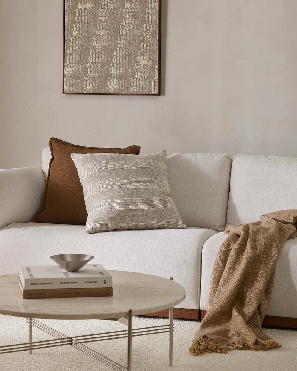 White sofa with brown and beige pillows and a blanket, accompanied by a round coffee table with decor items.