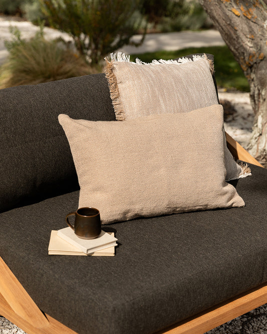 Beige pillow on a dark cushioned outdoor chair with a cup and napkin.
