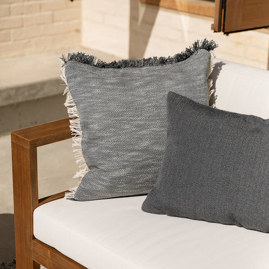 Wooden outdoor chair with white cushion and gray textured pillows against a stone wall.