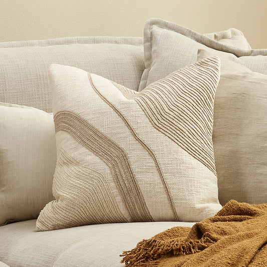 Beige sofa with textured pillows and a brown blanket on a neutral background