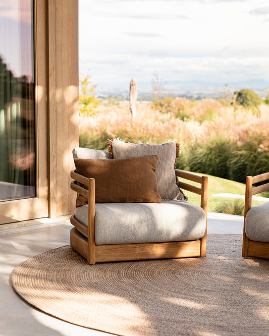 Wooden outdoor chair with cushions on a patio with a view of nature.
