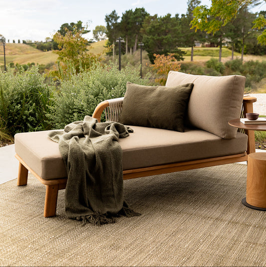 Outdoor sofa with cushions and a blanket in a garden setting