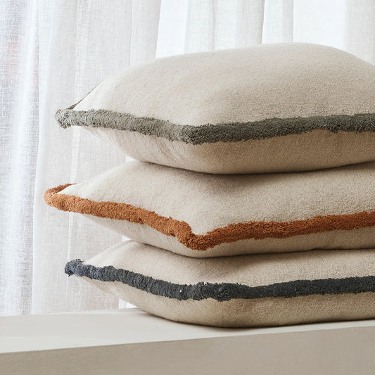 Stack of three decorative pillows with different color accents against a white curtain background