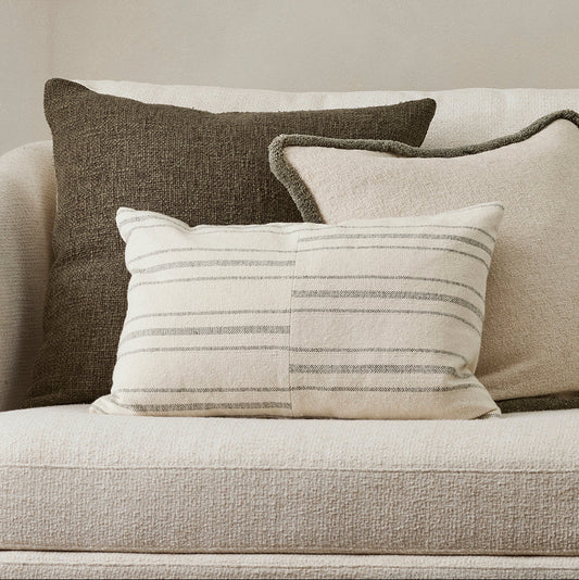 Three pillows on a beige sofa against a neutral wall