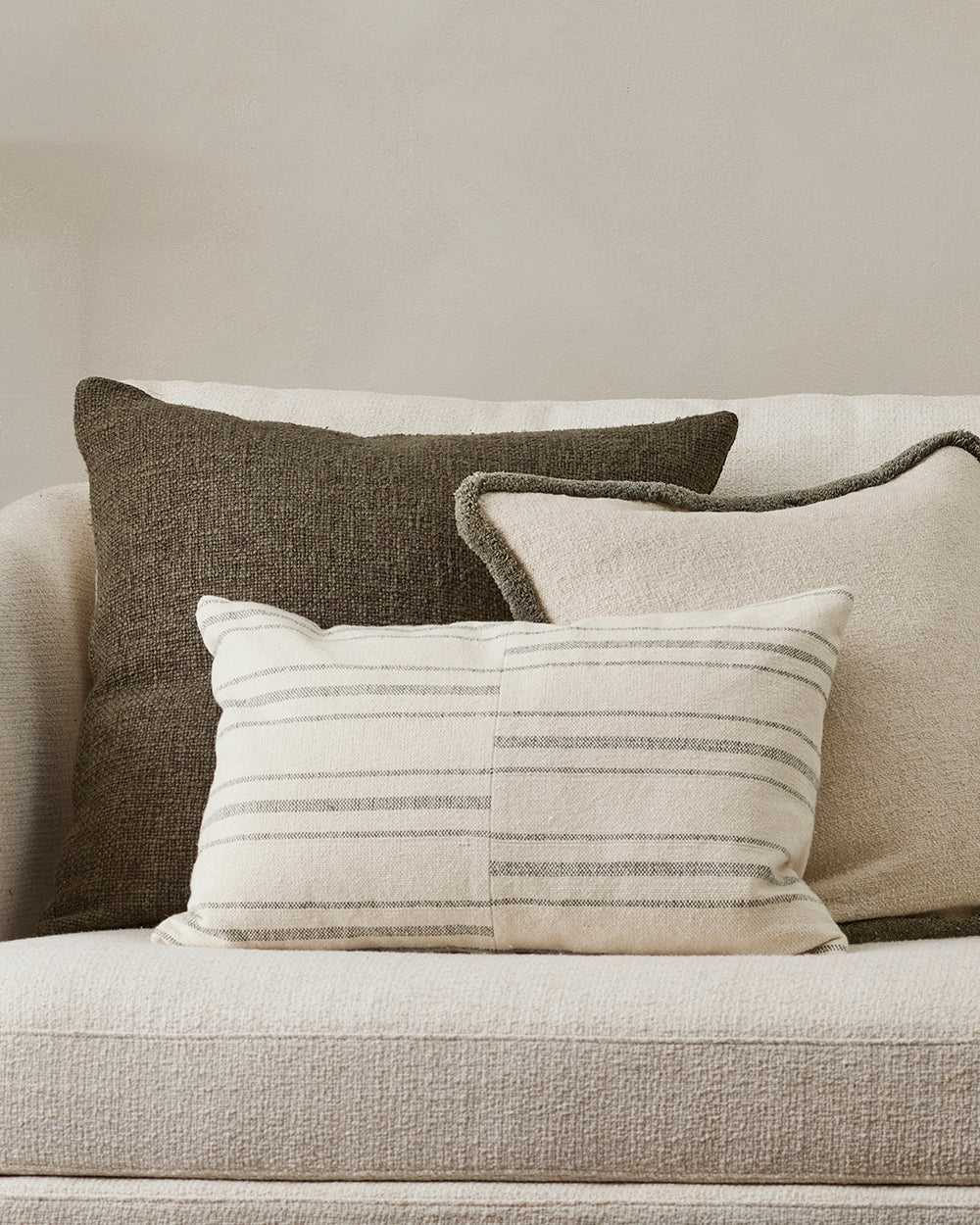 Three pillows on a beige sofa against a neutral wall