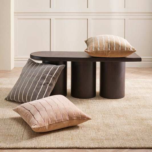 3 cushions positioned by brown modern coffee table on a cream rug with create wainscotting walls