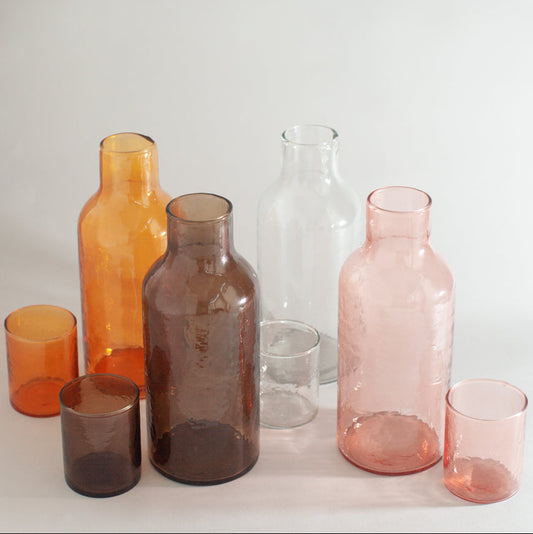 Set of colorful glass bottles and cups on a light background