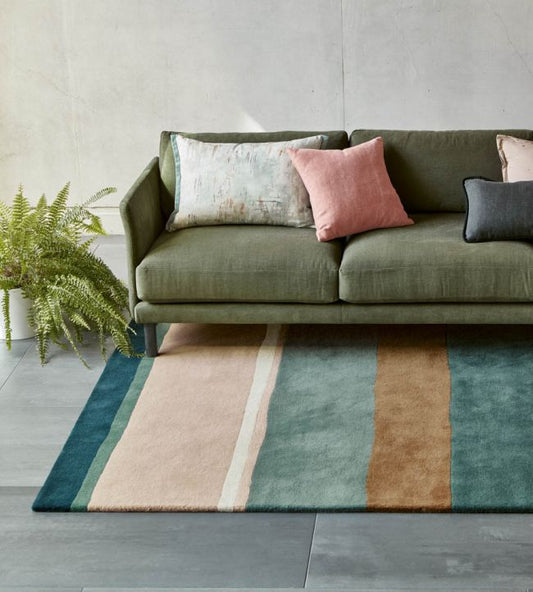 Green sofa with colorful cushions on a striped rug in a living room setting.