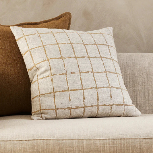 plain cream cushion with a ragged grid pattern design in ochre sitting on a cream sofa against a tobacco coloured plain cushion