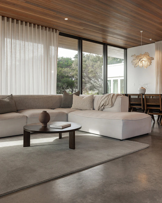 Modern living room with a sectional sofa, coffee table, and large windows.