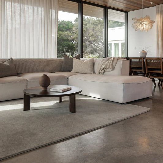 Modern living room with a sectional sofa, coffee table, and large windows.