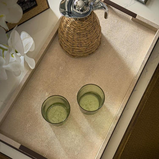 Two green glass tumblers on a textured surface with a woven container and white flowers in the background.