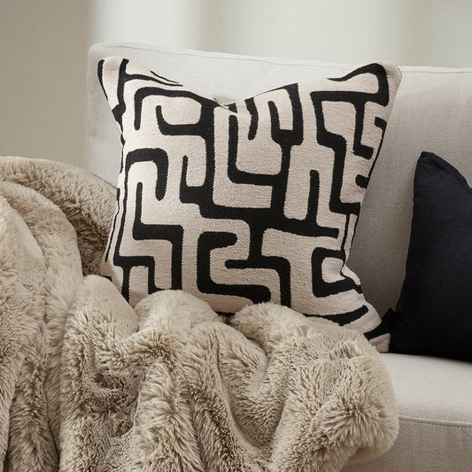 Decorative pillow with black geometric pattern on a light-colored sofa.