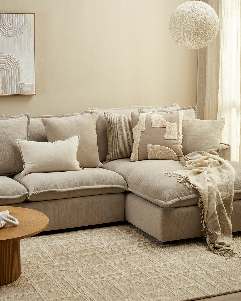 Beige sectional sofa with decorative pillows and a blanket in a living room setting.