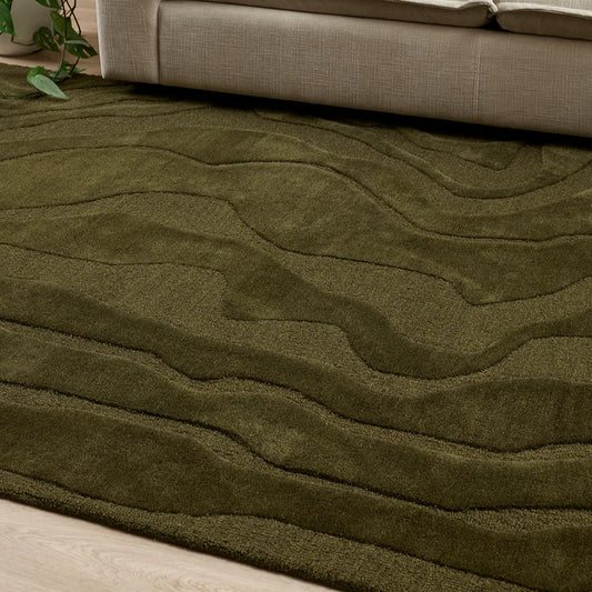 Green textured rug in front of a beige sofa with decorative pillows.