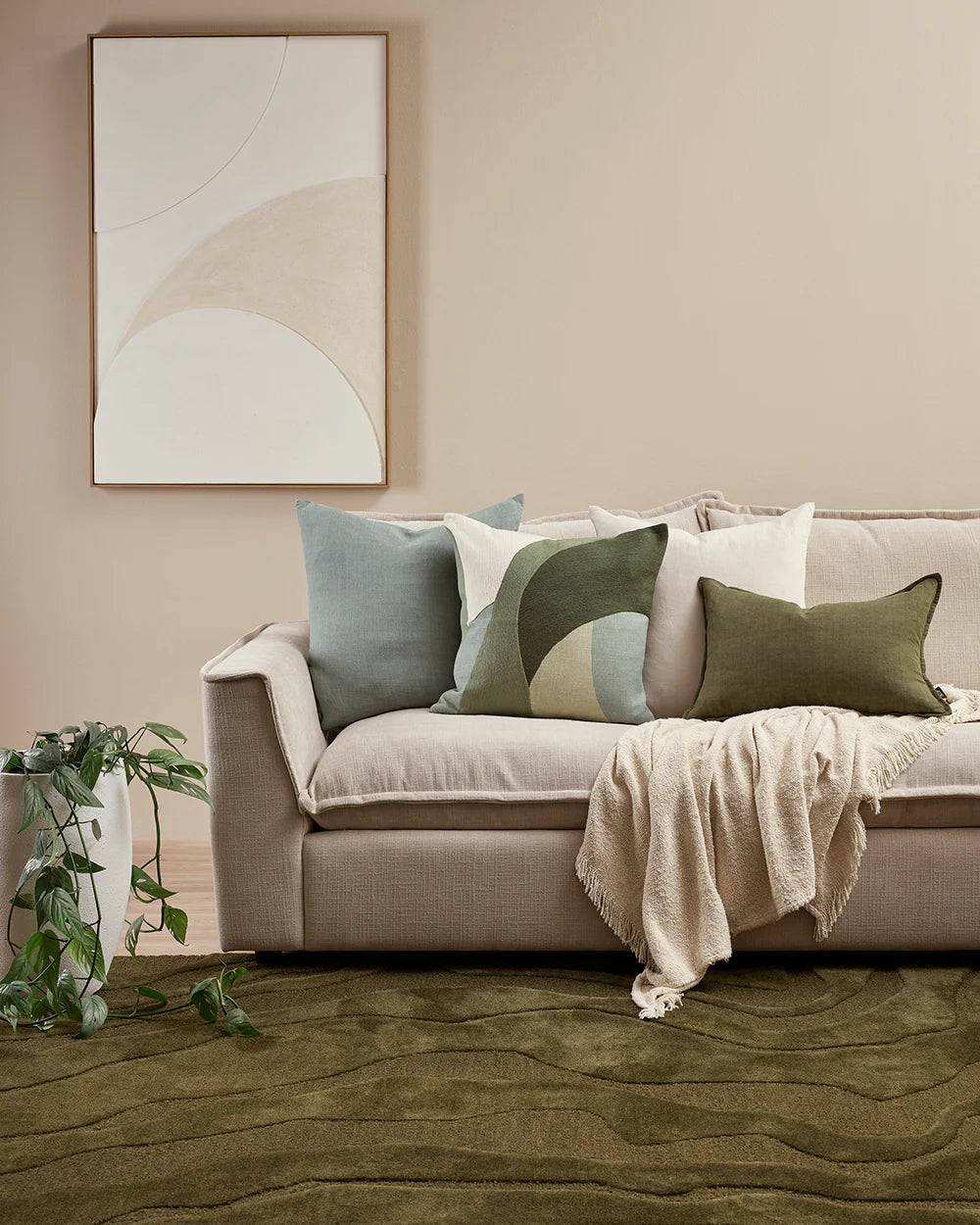 Beige sofa with decorative pillows and a blanket in a living room setting.