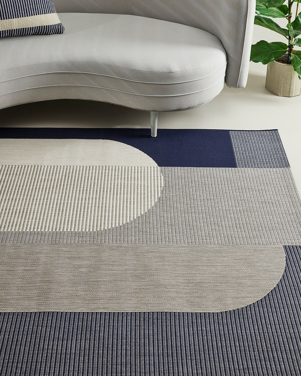 Gray and blue patterned rug in a living room setting with a sofa and plant.