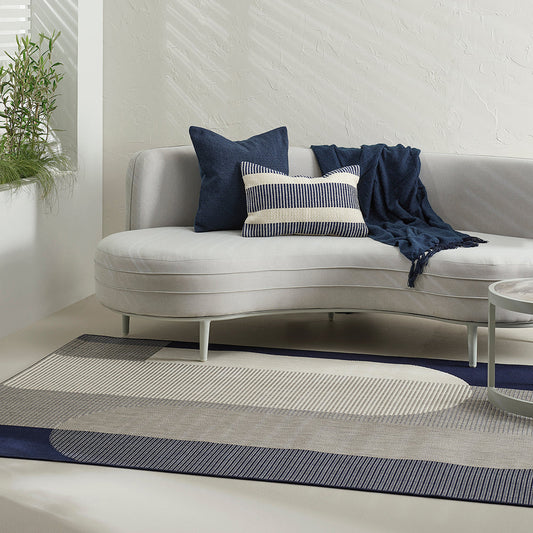 Modern living room with a curved sofa, cushions, and a rug.