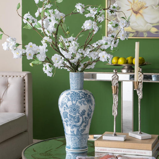 Decorative vase with white flowers on a table against a green wall with floral art.