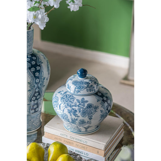Blue and white ceramic jar with floral patterns on a stack of books, with another similar jar in the background.