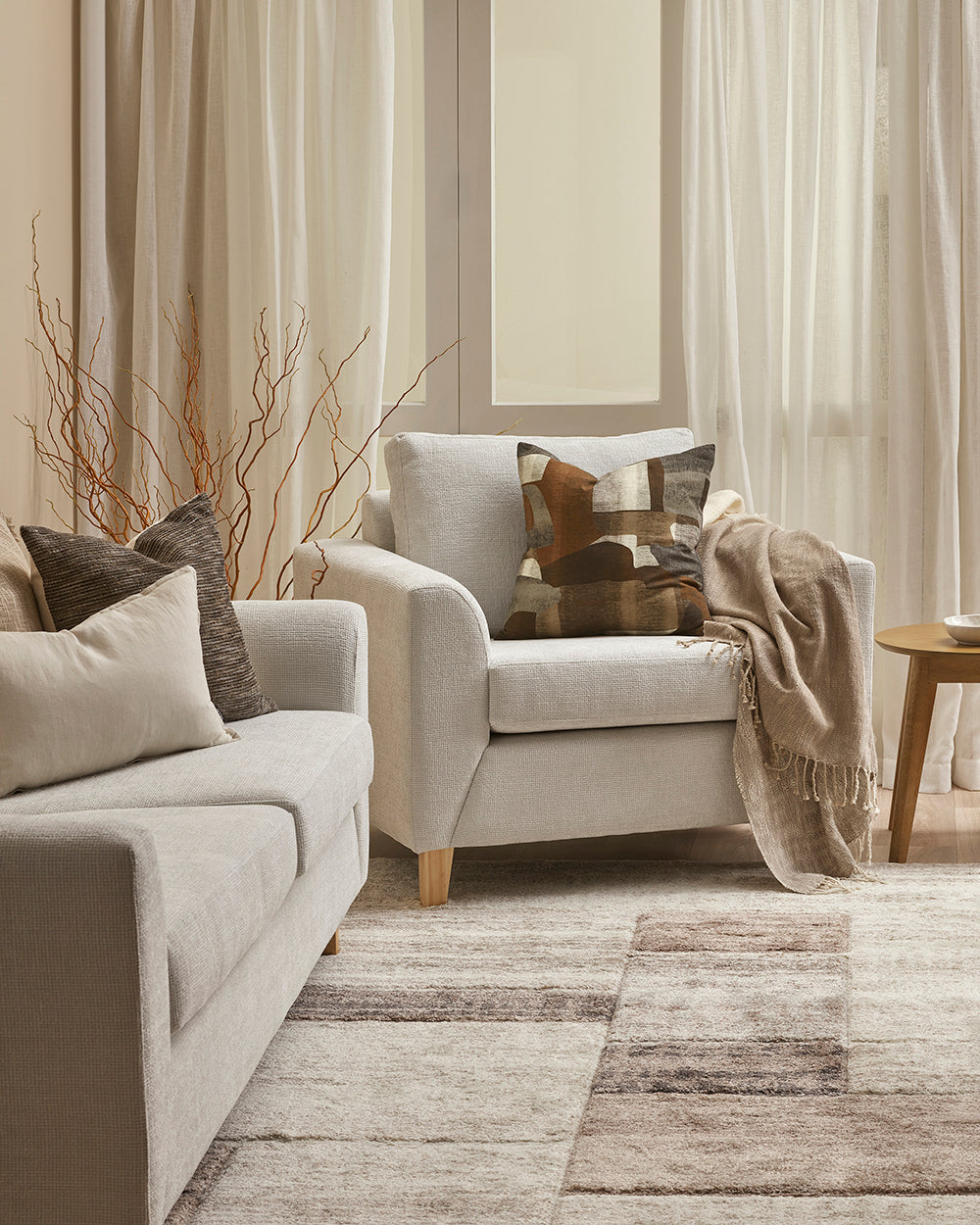Cozy living room with beige sofa and armchair, decorative pillows, and a wooden side table.