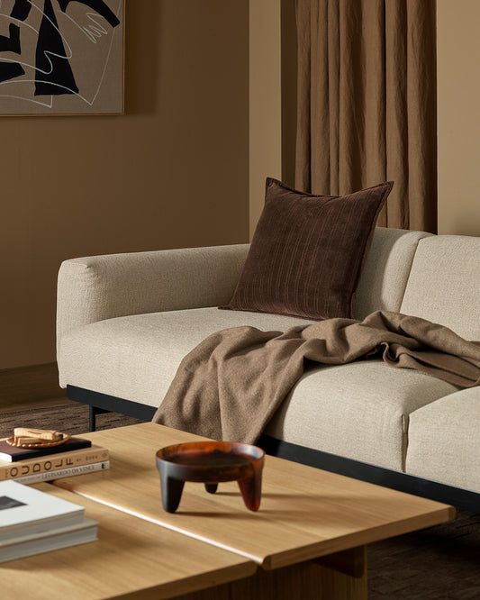 Beige sofa with a brown pillow and blanket in a living room setting.