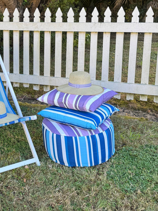 Blue and white striped chair and ottoman with matching pillows on grass, white picket fence in background