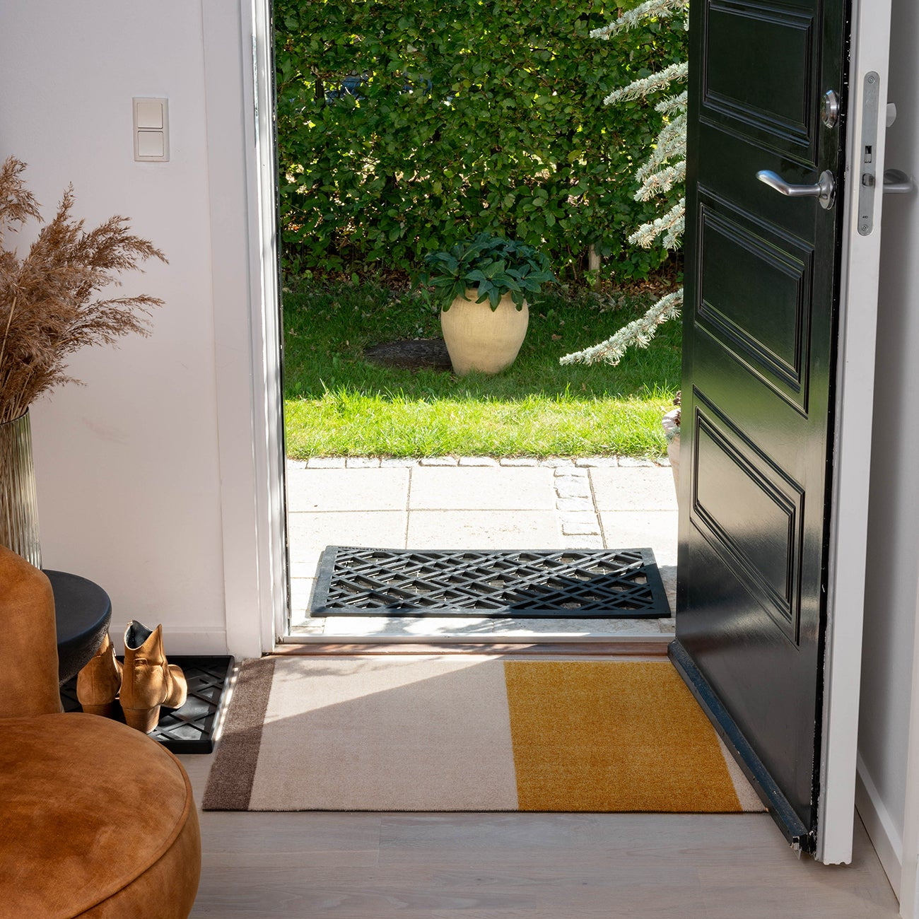 Open door leading to a garden with a rug on the wooden floor.