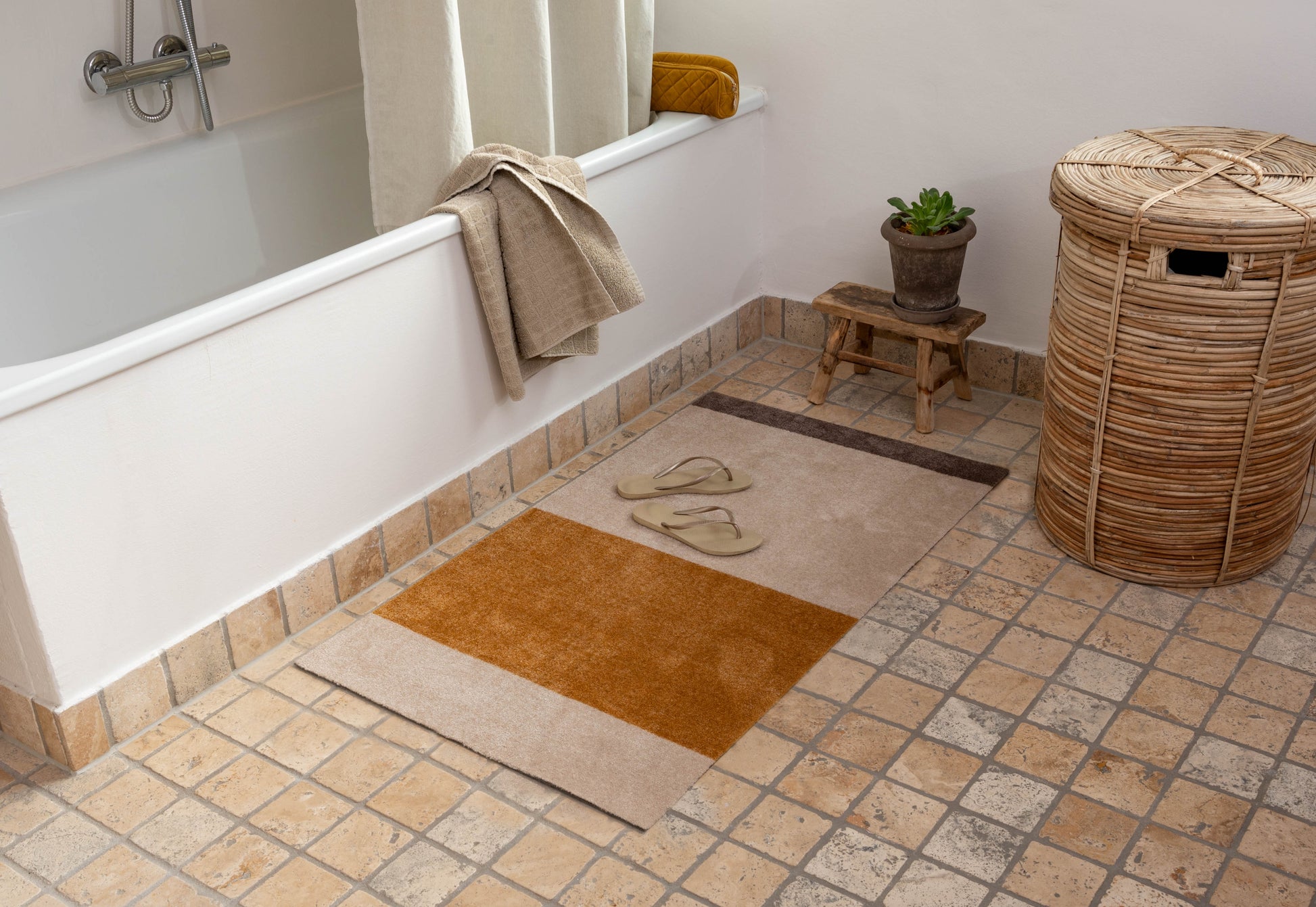 Bathroom with bathtub, rug, and laundry basket on tiled floor