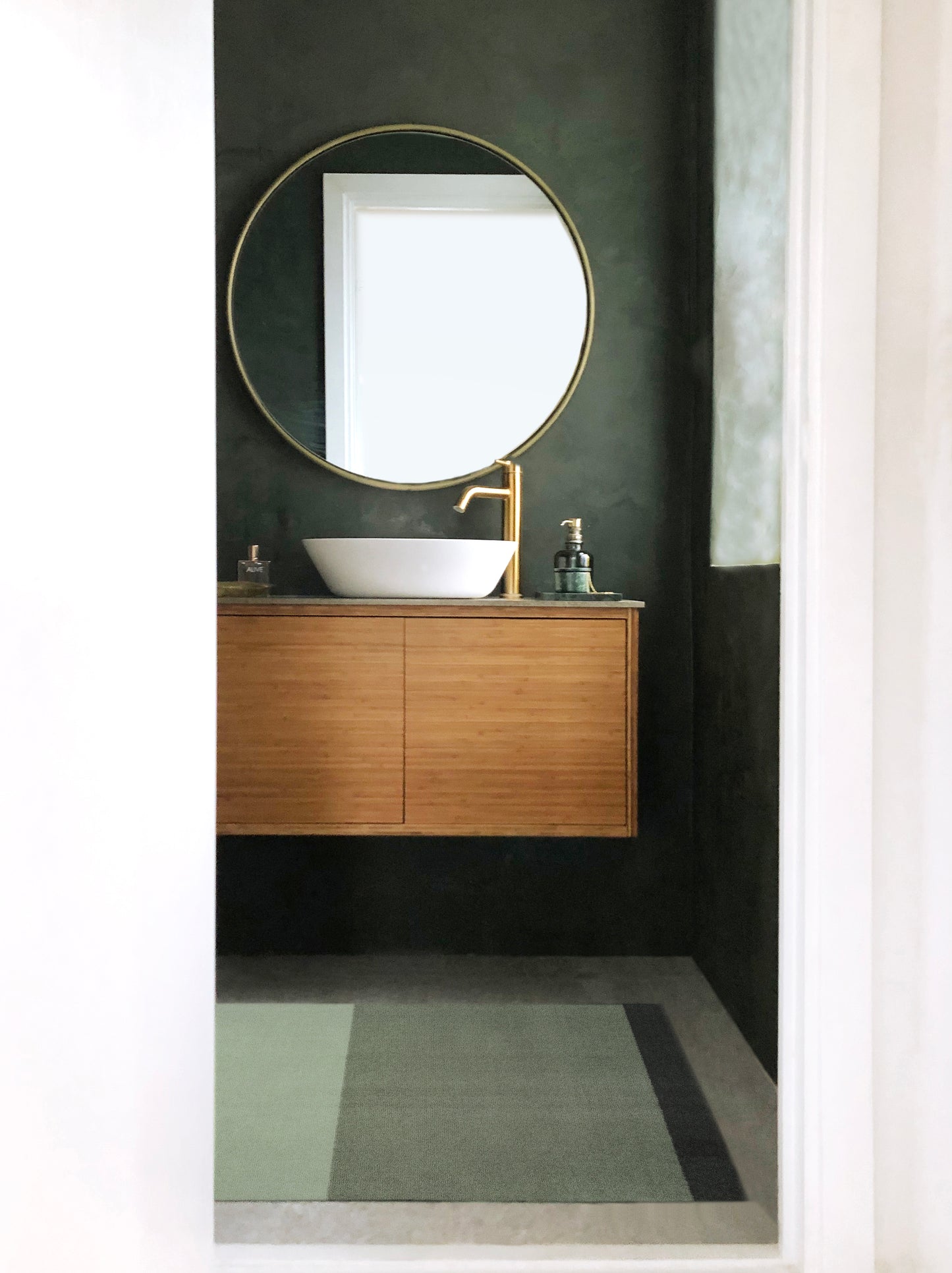 Bathroom vanity with round mirror and sink against a dark green wall.