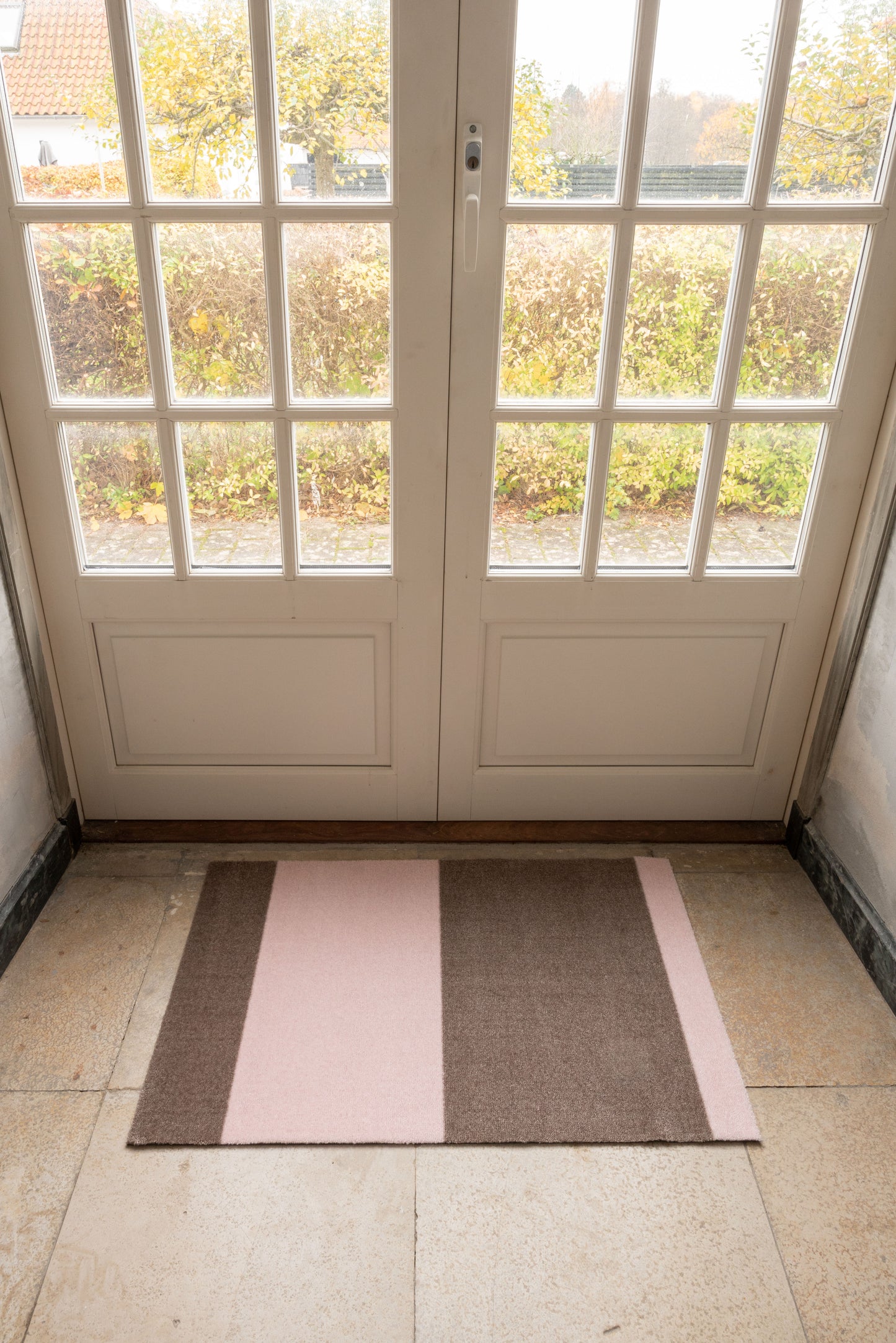 Rectangular rug with pink and brown stripes on a tiled floor in front of a glass door.