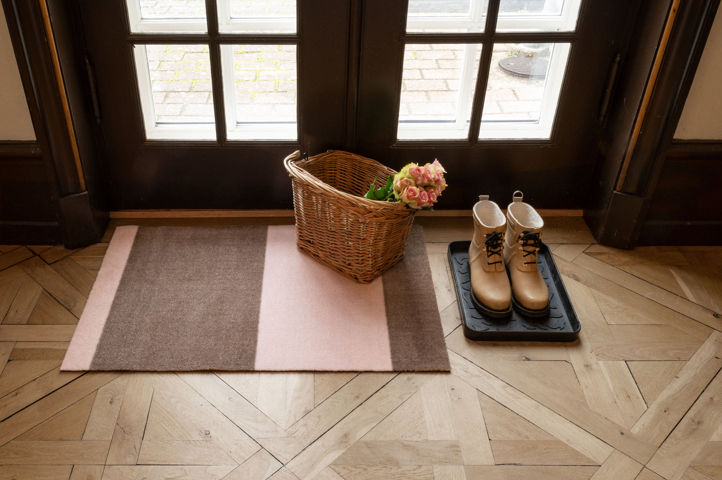 Wicker basket with flowers on a multicolored rug in front of a door.