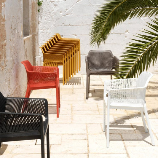 Nardi net chair - mustard, taupe, white, coral and charcoal, some stacked and the rest in a white stone courtyard with palm fronds